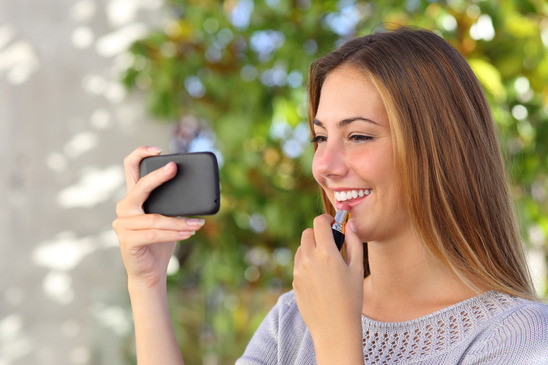 Beautiful woman making up using a smart phone as a mirror